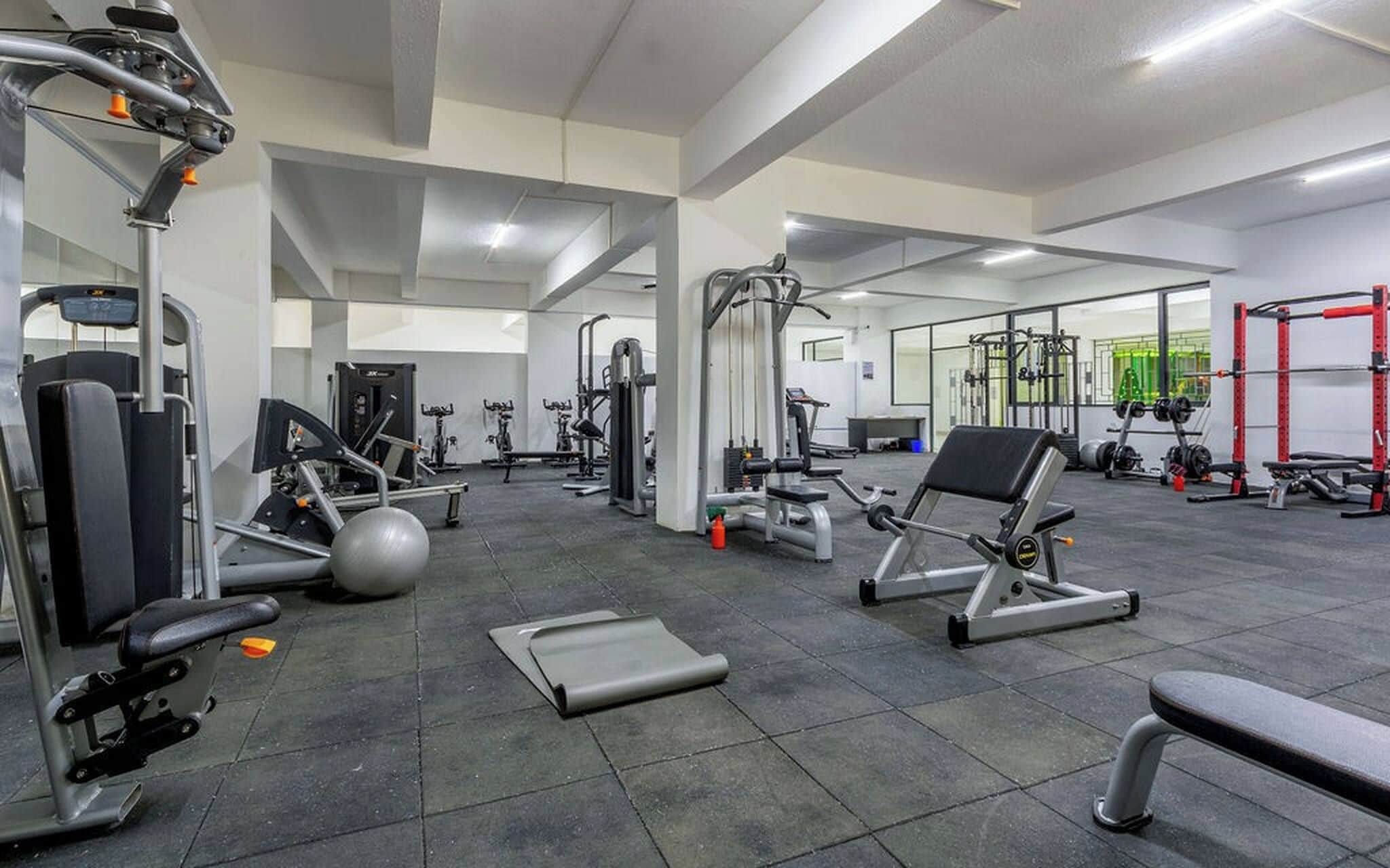 Un gimnasio con diversos equipos de ejercicio, incluyendo máquinas de pesas, pesas libres y máquinas de cardio.