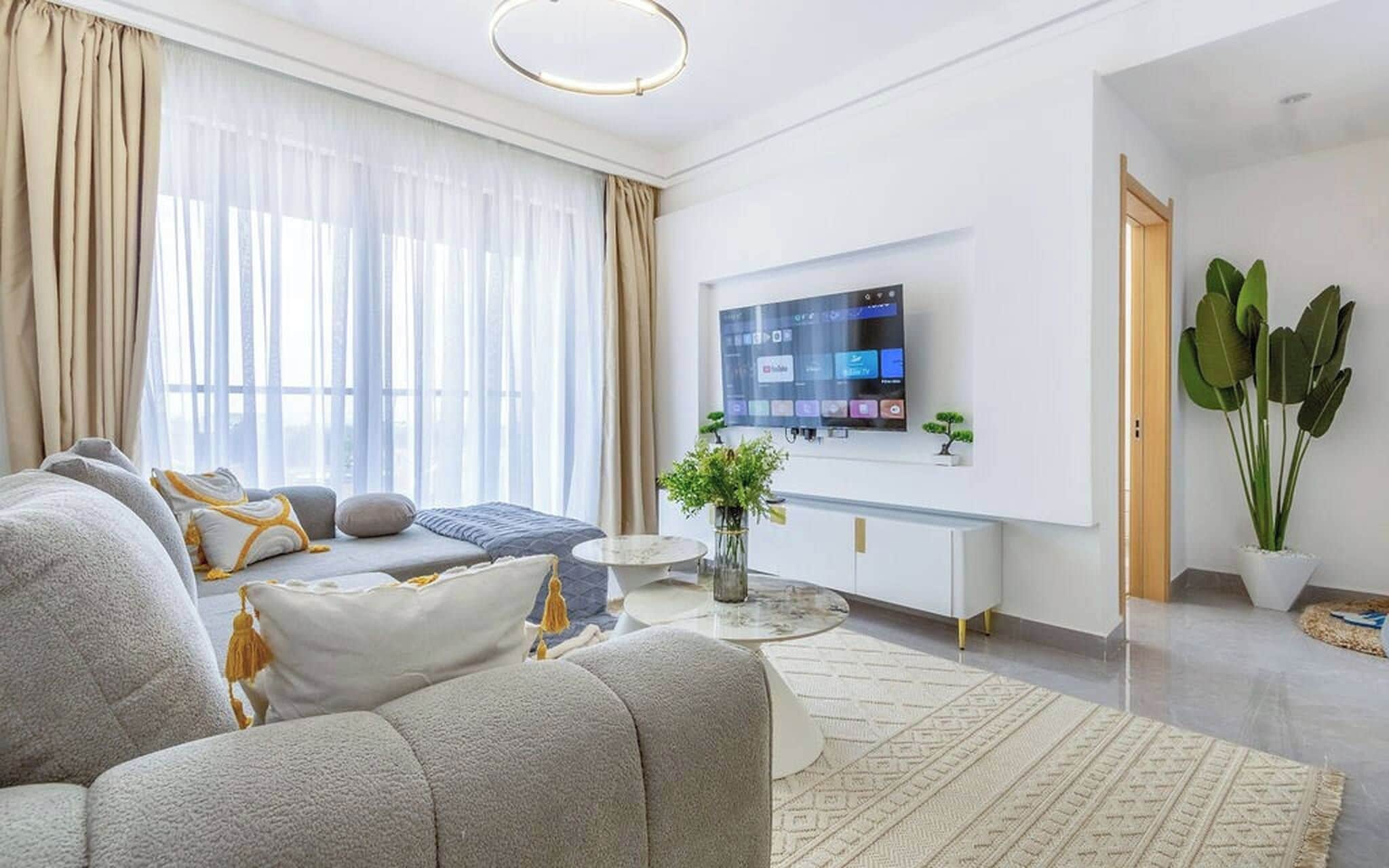 Una sala de estar moderna con un sofá, un televisor de pantalla plana montado en la pared y una planta en maceta.