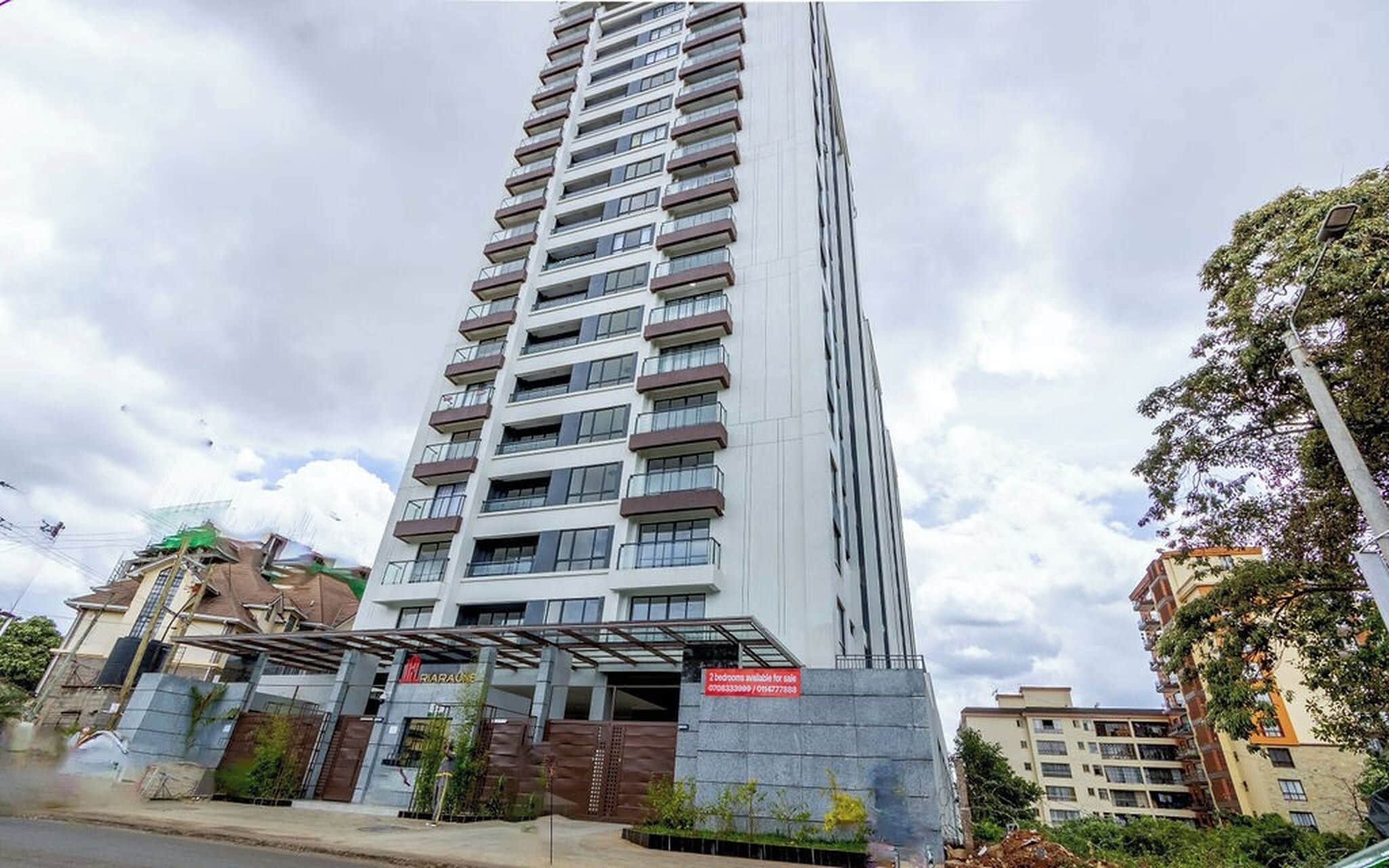 Un immeuble résidentiel à plusieurs étages, doté de balcons, d’une entrée sécurisée et d’un panneau indiquant les appartements disponibles à la vente.