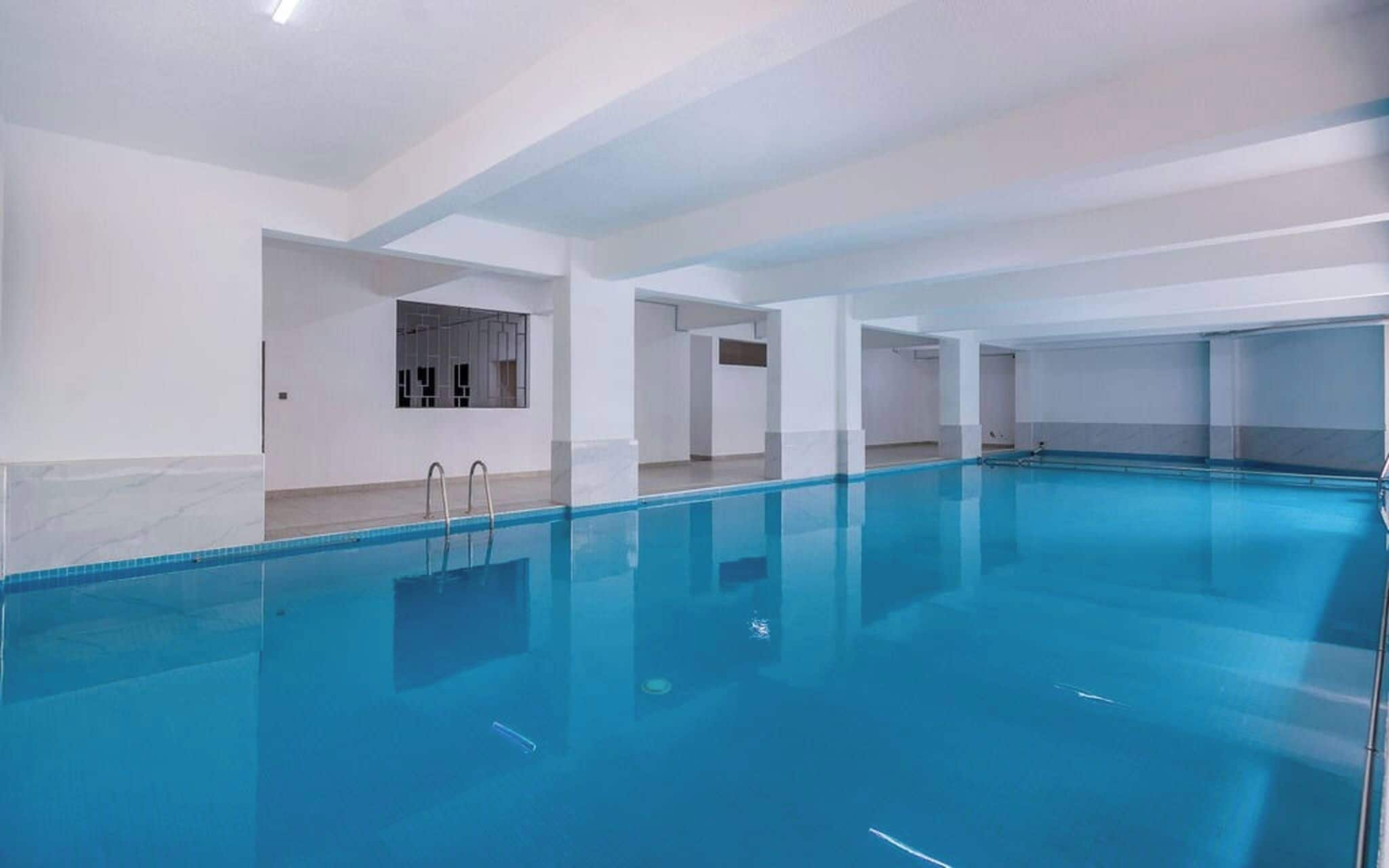 Une grande piscine intérieure à l’eau d’un bleu limpide, entourée de murs blancs et dotée d’un sol carrelé.