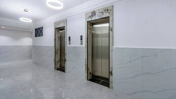 An interior with two elevators, marble flooring, and recessed ceiling lights.