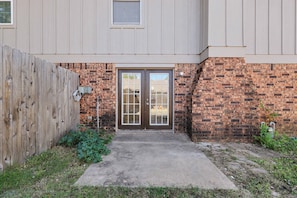 A residential building with a brick exterior, a wooden fence, and a concrete pathway leading to a double door entrance. - Prairie Meets Desert Modern 3BR Near OU (Norman)