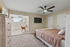 A bedroom with a bed, a desk, a chair, a wardrobe, a ceiling fan, and a television. - Prairie Meets Desert Modern 3BR Near OU (Norman)