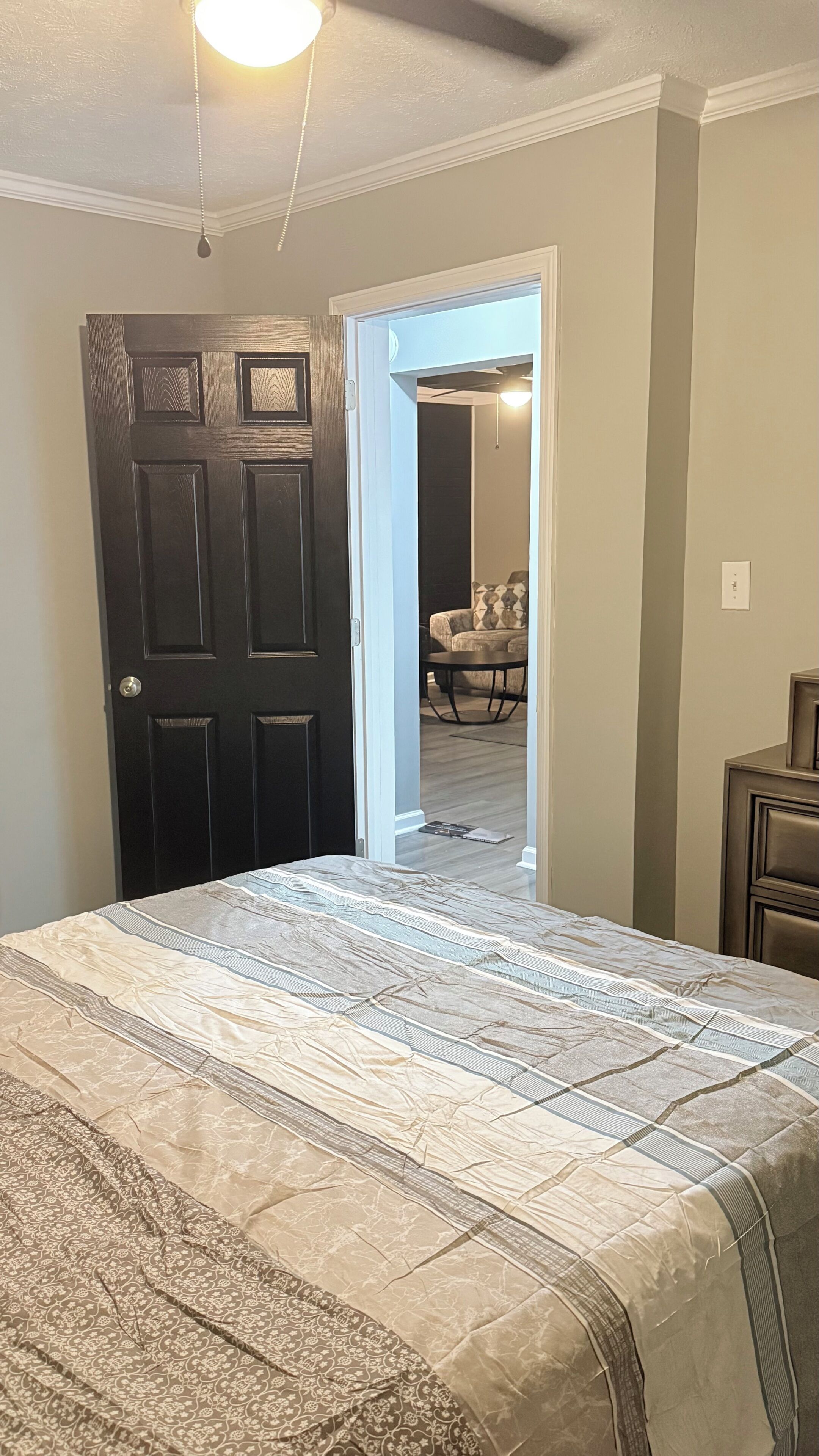 Un dormitorio con cama, una puerta y un acceso abierto a una sala de estar con sofá y mesa.