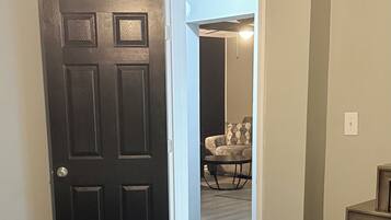 Un dormitorio con cama, una puerta y un acceso abierto a una sala de estar con sofá y mesa.