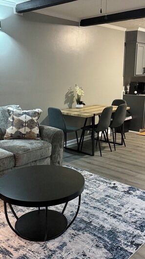 A modern living room with a sofa, a round coffee table, and a dining area with chairs and a table. - The Cove #3, Adorable 2-bedroom apartment with AC in Rockingham (Rockingham)