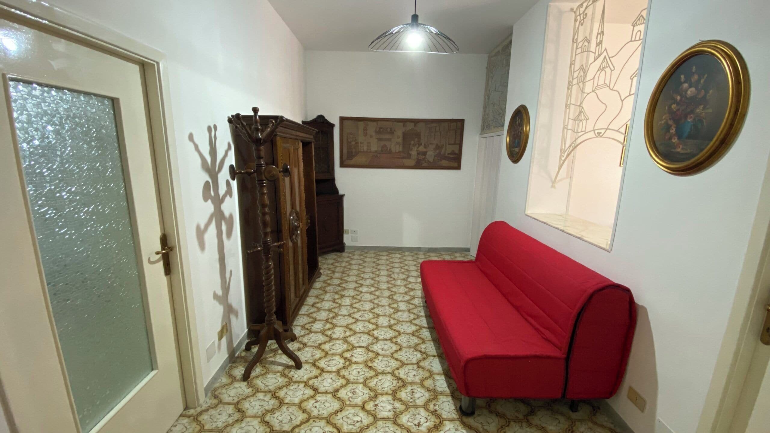 A hallway with a red sofa, a wooden cabinet, a wall-mounted painting, and a patterned floor.