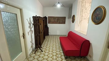 A hallway with a red sofa, a wooden cabinet, a wall-mounted painting, and a patterned floor.