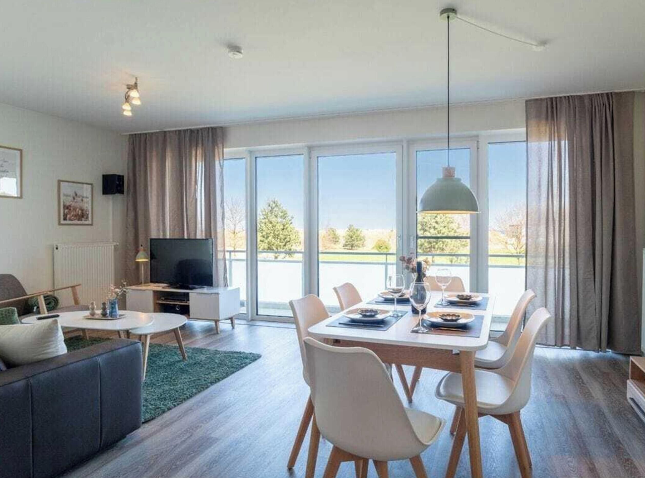 Een moderne woonkamer met een eetgedeelte, grote ramen en een flatscreen televisie.