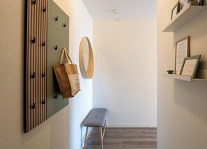 Een gang met een bankje, een spiegel aan de muur en een plank met ingelijste decoraties.