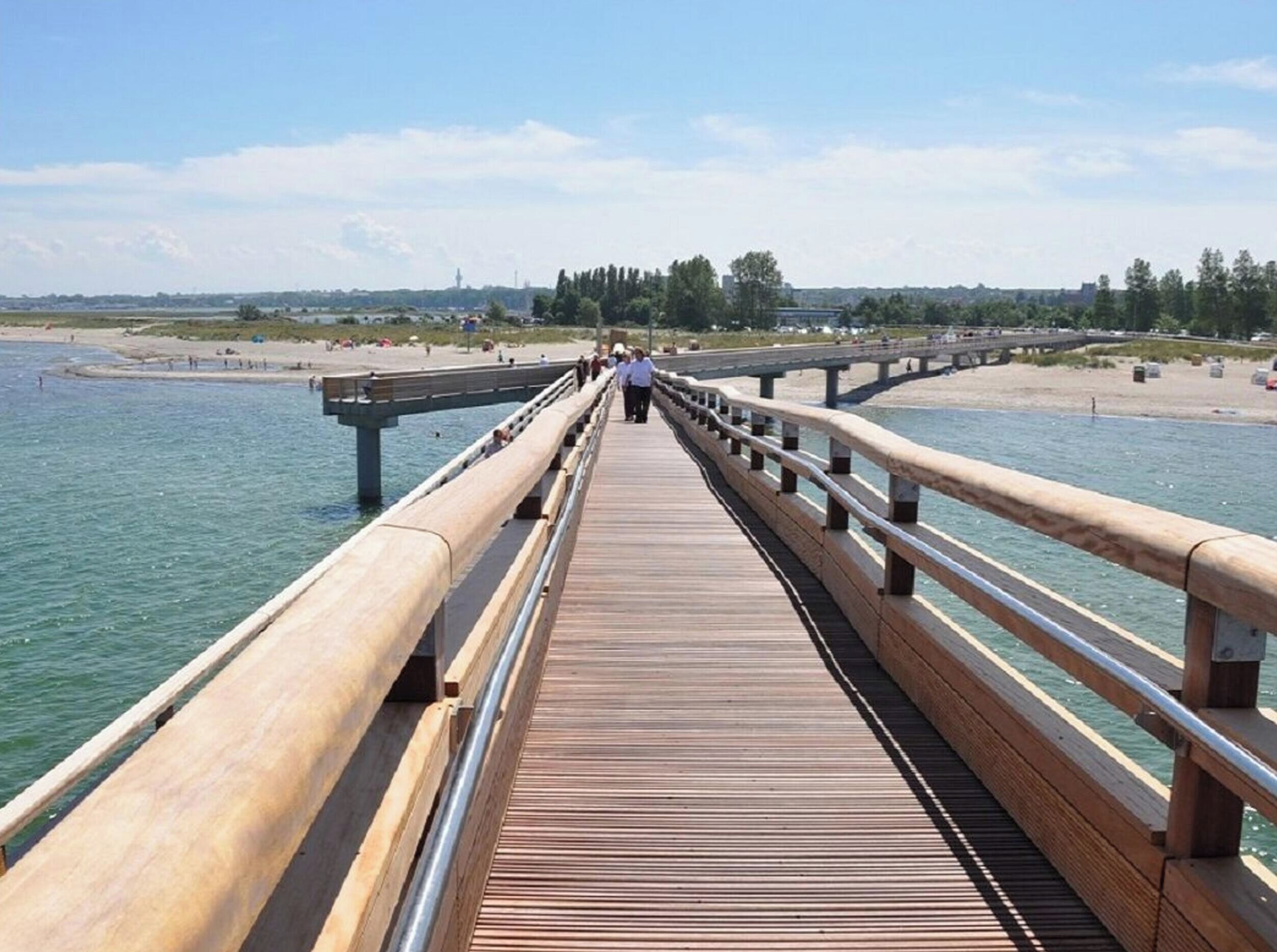 A wooden boardwalk leading to a beach with a clear view of the water and distant buildings.