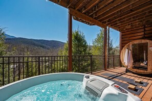 Un jacuzzi en una terraza de madera con vistas a un bosque y montañas.