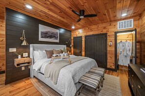 A modern bedroom with a large bed, bedside tables, a ceiling fan, and a view of the outside. - Radford Place~ A Couples Retreat (Gatlinburg)