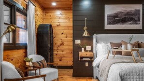 Ein gemütliches Zimmer mit Bett, Stuhl, kleinem Tisch und einer Wandregal.