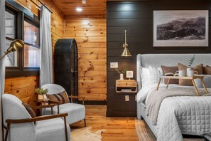 Una habitación acogedora con una cama, una silla, una mesita y un estante en la pared.