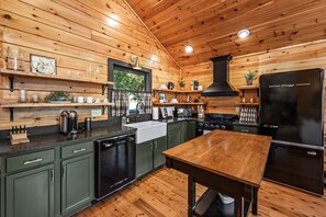 A kitchen with wooden walls, a black stove, a black refrigerator, and a wooden table. - Radford Place~ A Couples Retreat (Gatlinburg)