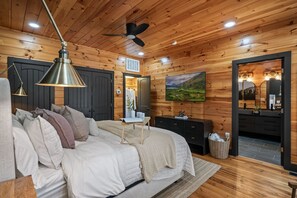 A wooden-paneled bedroom with a bed, bedside table, lamp, and a painting on the wall. - Radford Place~ A Couples Retreat (Gatlinburg)