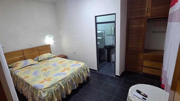 A small bedroom with a bed, a nightstand, a mirror, and a door leading to a bathroom. - Ximena's House: It offers the space and freedom your family needs. (Iquitos)