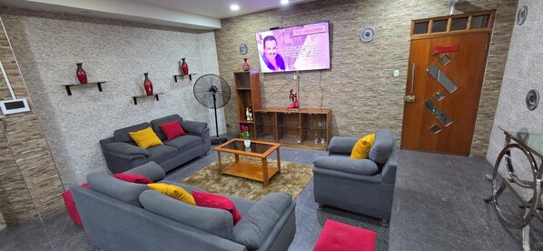 Sala de estar com sofás cinzas, uma mesa de centro e uma televisão fixada na parede.