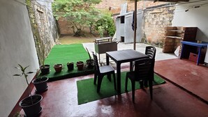A patio area with a table and chairs, potted plants, and a green turf. - Ximena's House: It offers the space and freedom your family needs. (Iquitos)