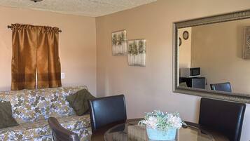 A dining area with a round glass table, four chairs, a ceiling fan, and two wall-mounted paintings.