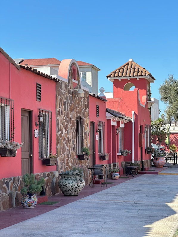 A row of buildings with red walls and stone accents, featuring balconies with potted plants. - Misión Boutique (Ensenada)