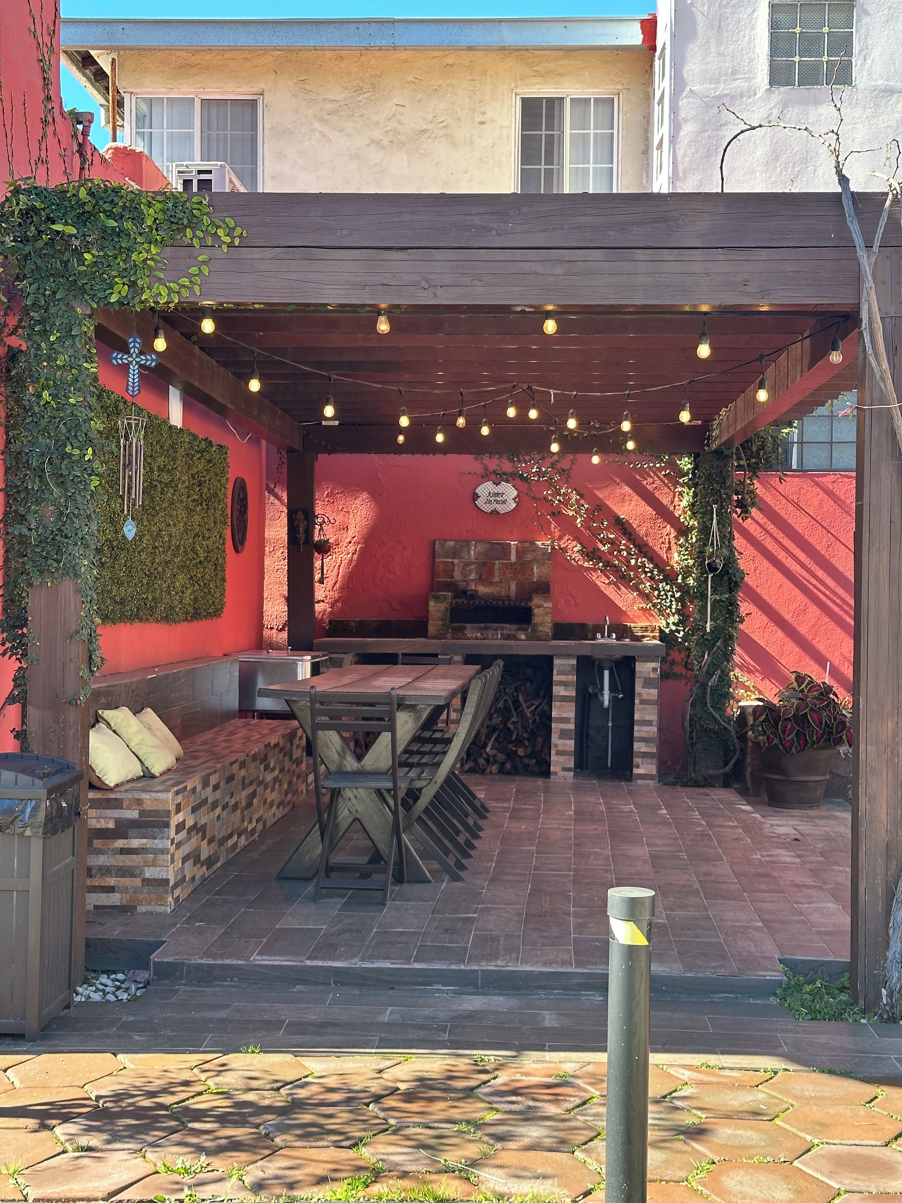 An outdoor patio with a wooden table and benches, a stone fireplace, and string lights.