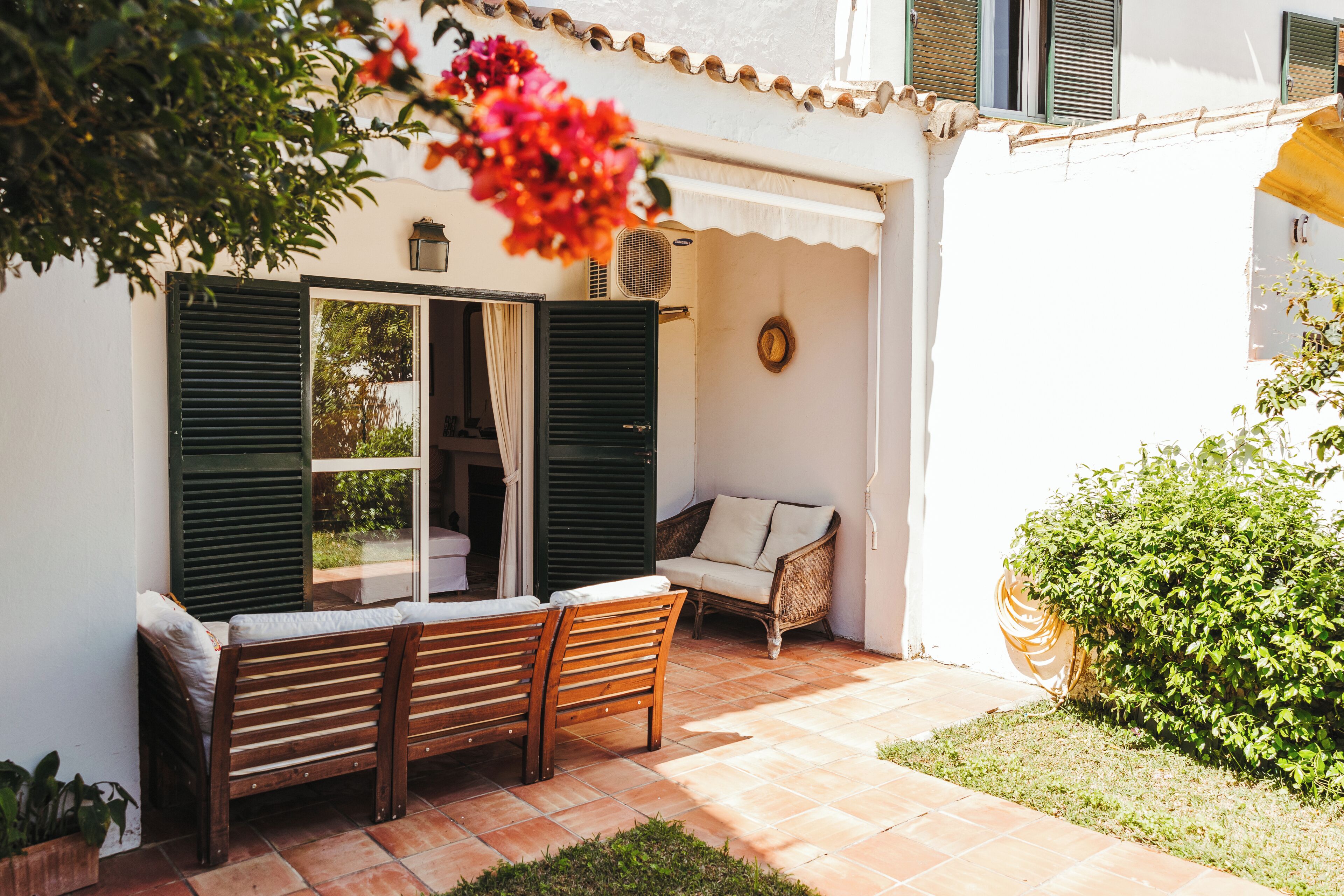 An outdoor seating area with a bench and a sofa, a door with shutters, and a potted plant.