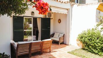 An outdoor seating area with a bench and a sofa, a door with shutters, and a potted plant.