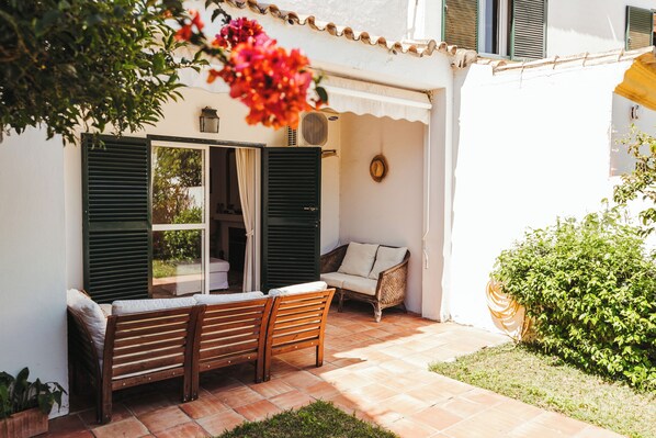Un espace extérieur aménagé avec un banc et un canapé, une porte avec des volets et un pot de fleurs.