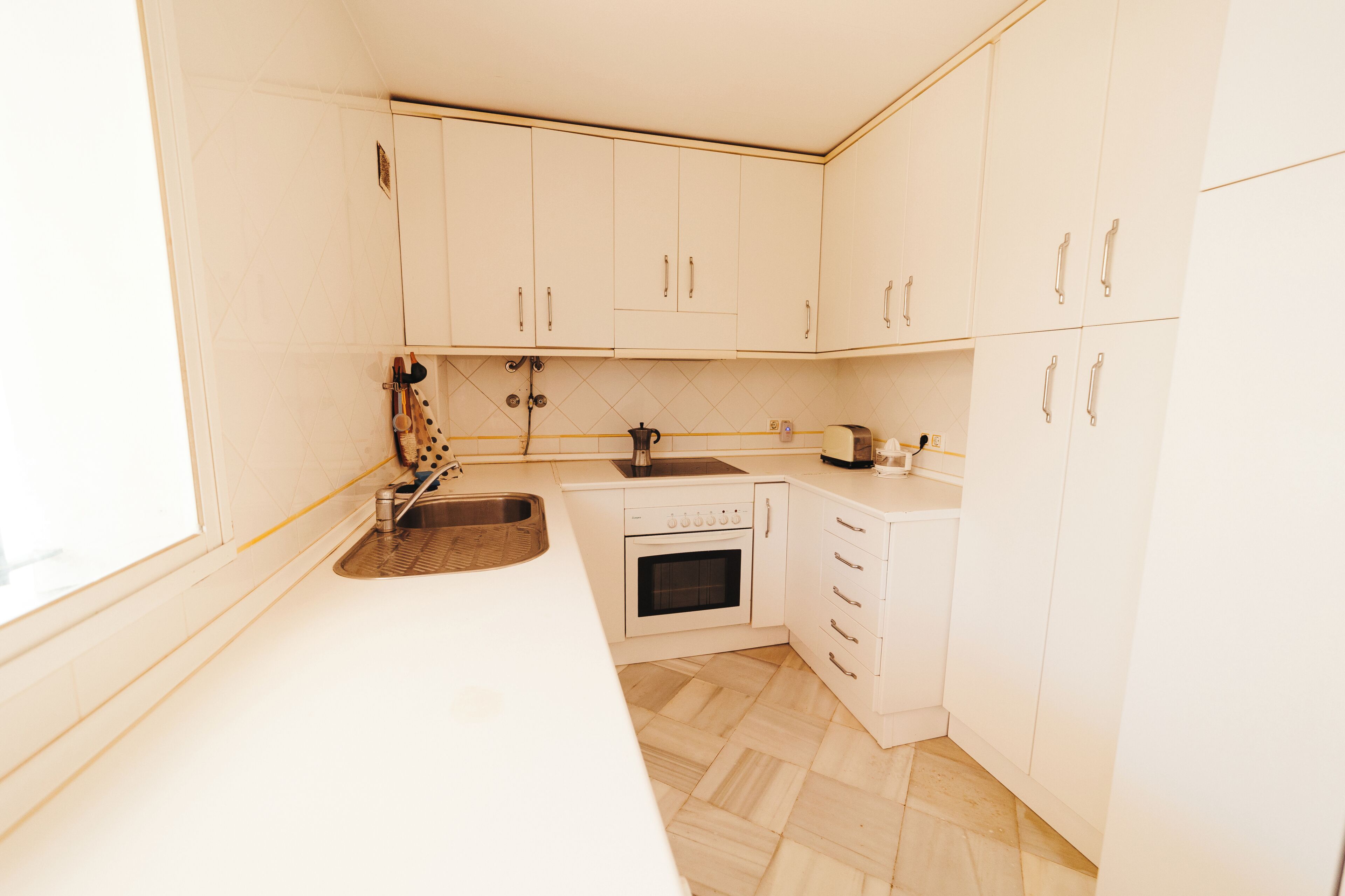 A kitchen with white cabinets, a stainless steel sink, a stove, and a toaster.