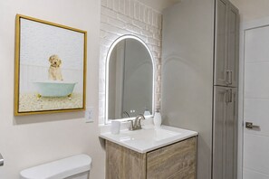 Een badkamer met een wit wastafelmeubel, een spiegel, een toilet en een lijst met een foto van een hond in bad.