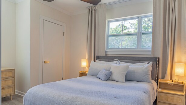 Ein Schlafzimmer mit einem Bett, zwei Nachttischen, einem Fenster mit Vorhängen und einer Tür.