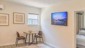Ein Zimmer mit einem Bett, einem Tisch mit Stühlen, einem Fenster und einem an der Wand befestigten Fernseher.