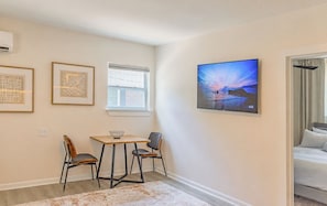 Een kamer met een bed, een tafel met stoelen, een raam en een aan de muur bevestigde televisie.