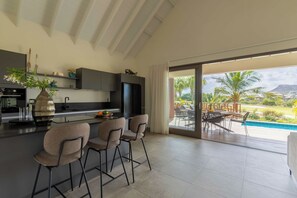 Una cocina moderna con una isla grande, taburetes de bar y vistas a una piscina y un área de estar exterior.