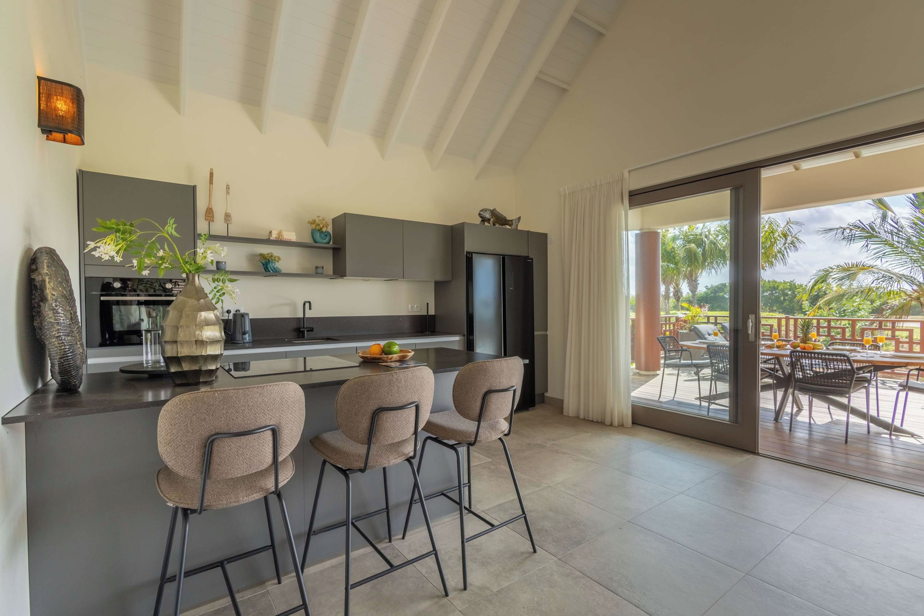 A modern kitchen with a central island, bar stools, and a view of the outdoor patio area.