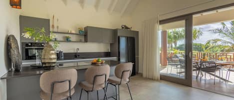 A modern kitchen with a central island, bar stools, and a view of the outdoor patio area.