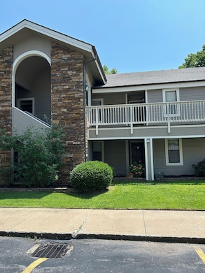A two-story building with a stone facade, a balcony on the second floor, and a small front yard with a bush and flowers. - 2BR/2BA Taneycomo Lake Views +Resort Perks + Pet Friendly (Branson)