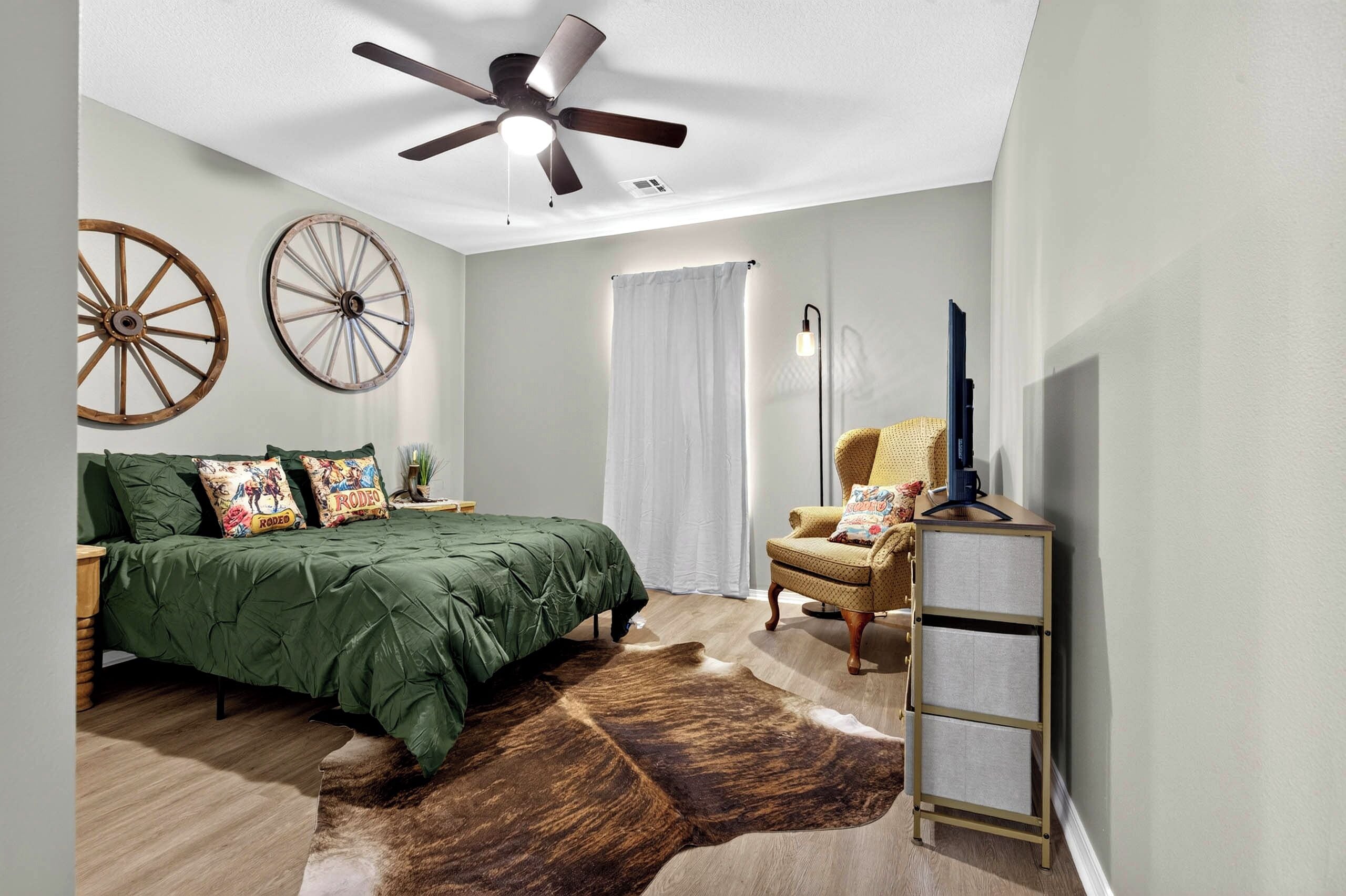 A bedroom with a bed, a chair, a ceiling fan, and a cowhide rug.