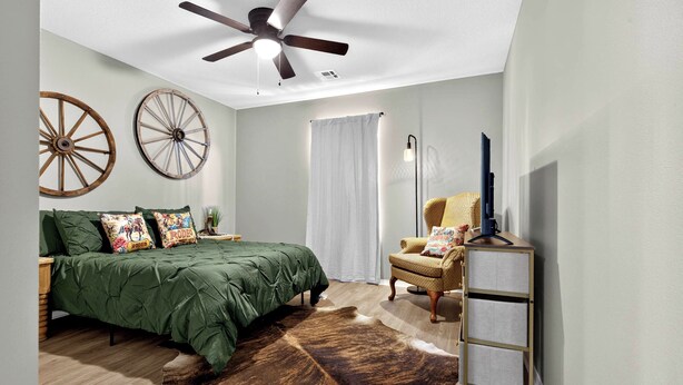 A bedroom with a bed, a chair, a ceiling fan, and a cowhide rug.
