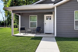 A single-story house with a covered porch, a front door, and two chairs.