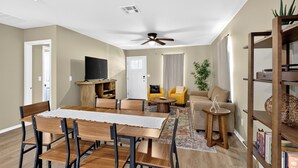 A modern living room with a dining area, a ceiling fan, and a bookshelf.