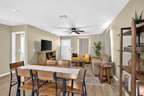 A modern living room with a dining area, a ceiling fan, and a bookshelf.