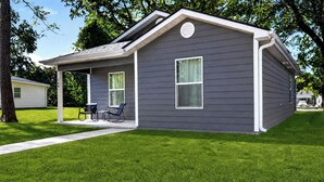 A single-story house with a covered porch, two windows, and a small patio with outdoor furniture.
