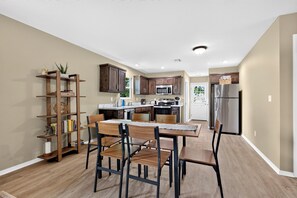 A modern kitchen with wooden cabinets, a dining table with chairs, and a built-in bookshelf.
