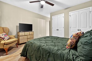 A bedroom with a bed, a dresser, a television, and a ceiling fan.
