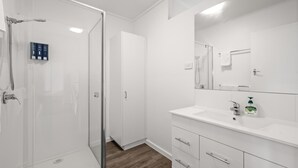 A modern bathroom with a glass shower enclosure, a white vanity with a mirror, and a wooden floor. - Phillip Island Cottage 1 (Cowes)