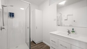 A modern bathroom with a glass shower enclosure, a white vanity with a mirror, and a wooden floor. - Phillip Island Cottage 1 (Cowes)
