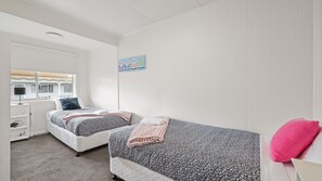 Un dormitorio con dos camas, una ventana, un radiador y una obra de arte colgada en la pared.